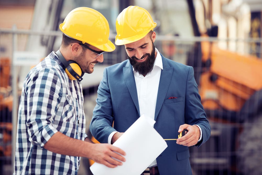 Two workers with hard hats standing in front of construction machinery looking at a drawing